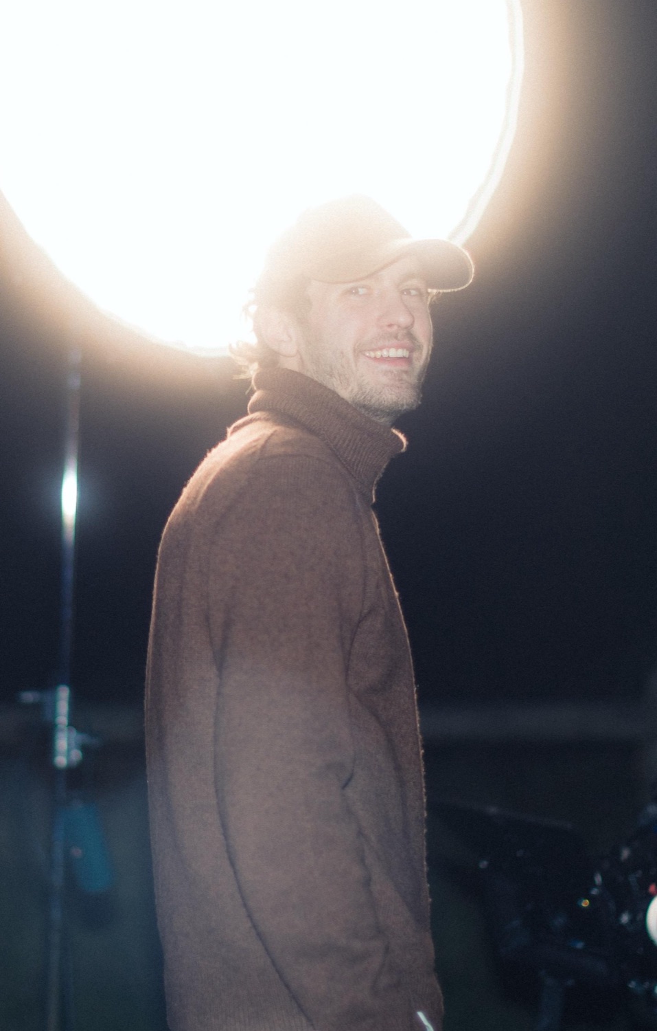 Je souris à contre-jour devant un projecteur, casquette sur la tête, sur un plateau de tournage de nuit