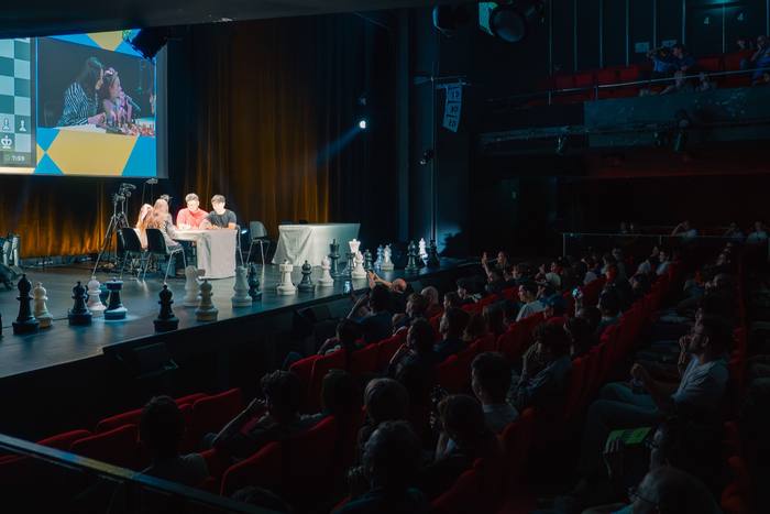 Salle comble vue depuis la scène, écran géant et pièces d’échecs surdimensionnées