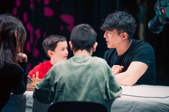 Trois joueurs concentrés autour de la table, décor rose en arrière-plan