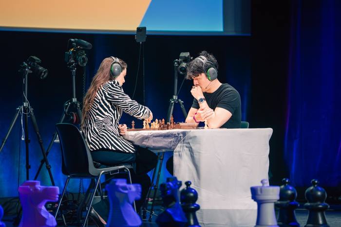 Duel sous casques antibruit dans une lumière bleue, caméras autour de la table