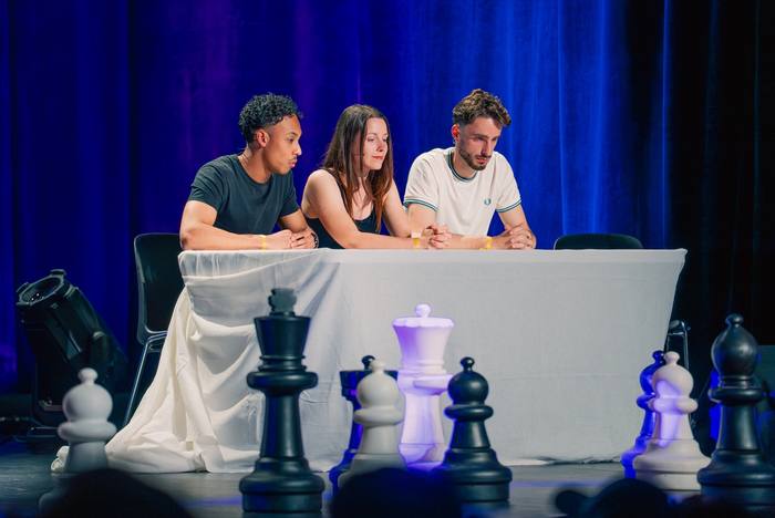 Trois personnes accoudées à la longue table blanche devant un rideau bleu