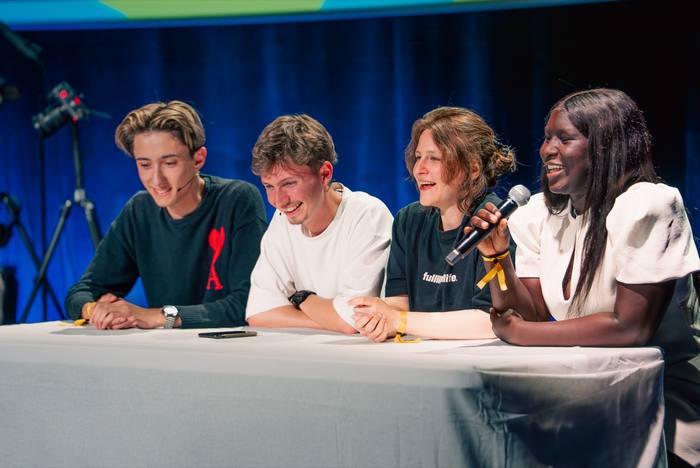 Quatre invités souriants derrière la table de jeu, micro à la main