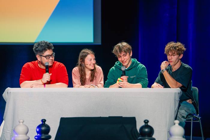 Cinq participants alignés derrière la table blanche devant l’écran coloré