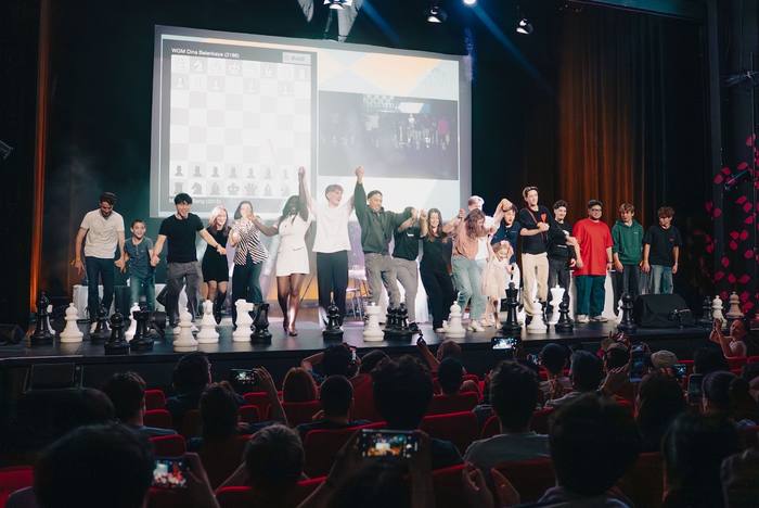 Toute la troupe saute de joie au salut final, pièces d’échecs géantes au bord du plateau et public smartphones levés