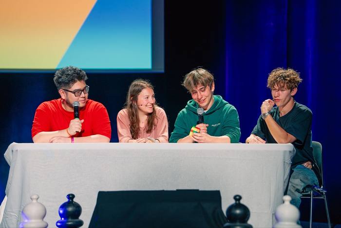 Quatre intervenants au micro derrière la table nappée, pièces d’échecs géantes au premier plan