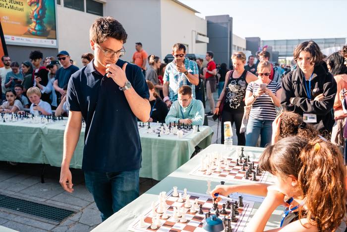 Arbitre debout, la main devant la bouche, entre les tables de jeu