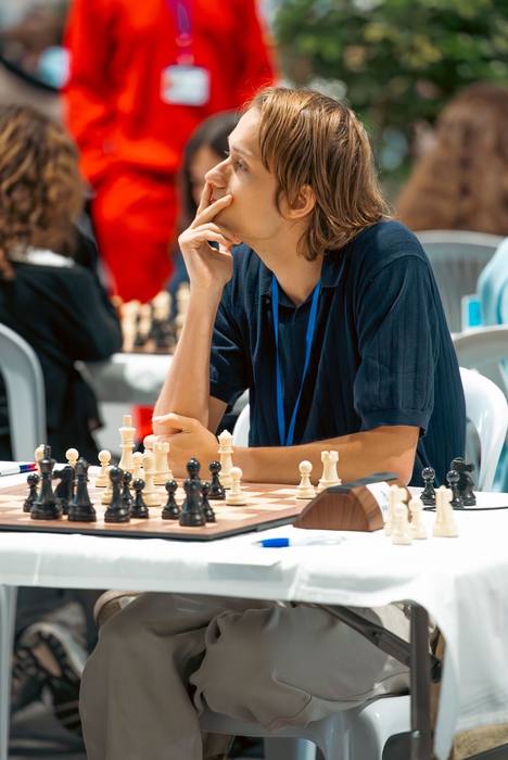 Joueur en polo bleu, badge autour du cou, le doigt sur la lèvre pendant sa réflexion