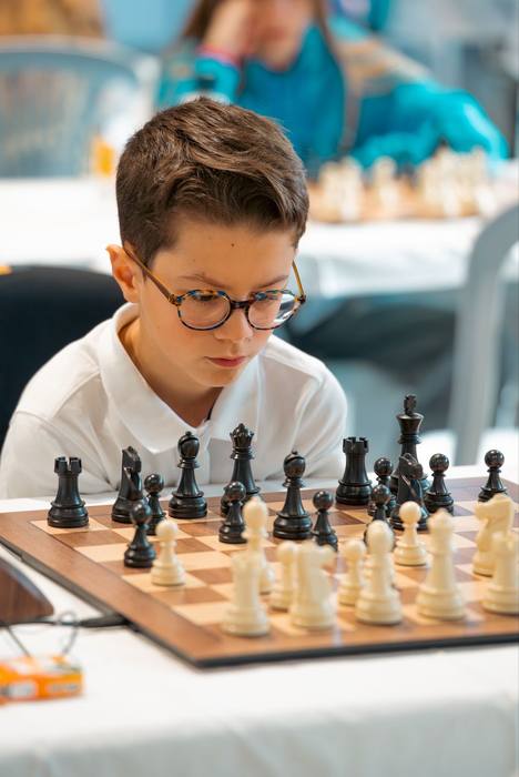 Jeune garçon à lunettes écaille fixant les pièces noires alignées devant lui