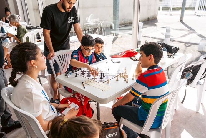 Table de jeunes joueurs encadrés par un coach dans la véranda vitrée, sacs rouges de la Fédération au sol