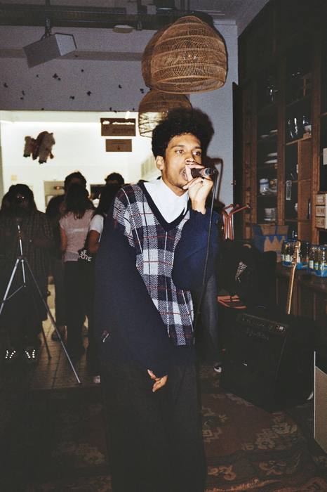 Chanteur au micro au milieu de la salle, pied de perche et amplis derrière lui, photo argentique