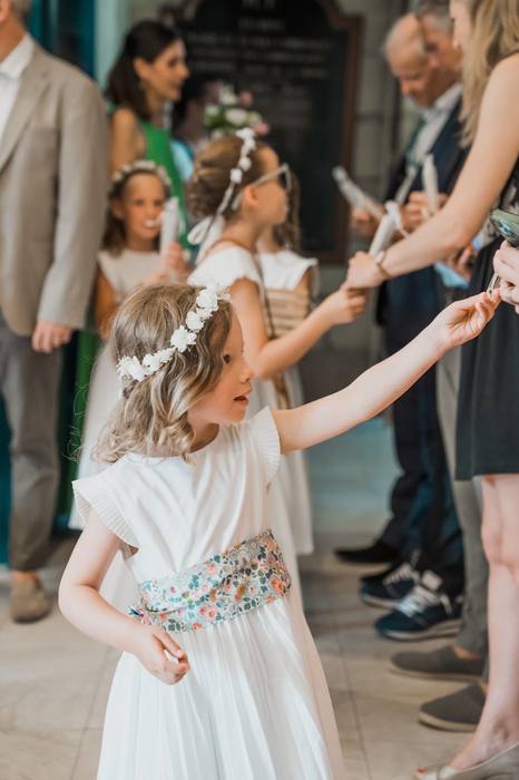 Petite fille couronnée de fleurs tendant la main aux invités