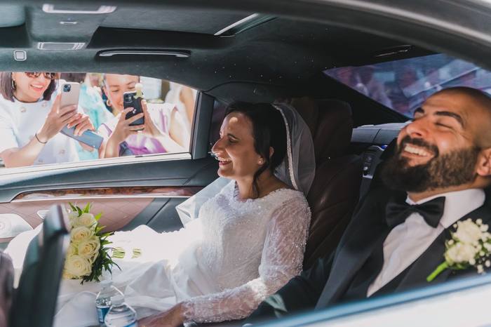 Les mariés riant dans la voiture, invités photographiant à travers la vitre