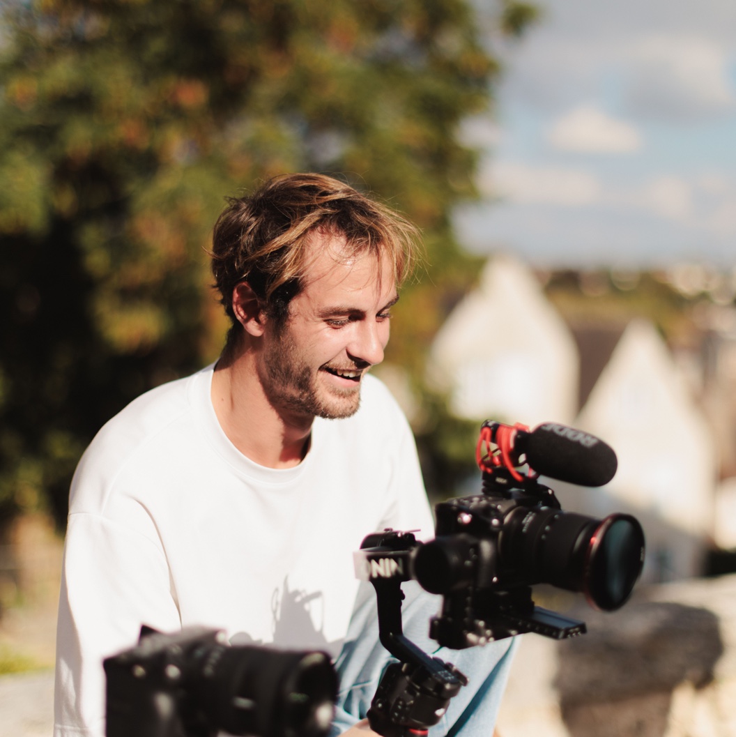 Ambrose Ducable, souriant, sa caméra à la main sur un tournage